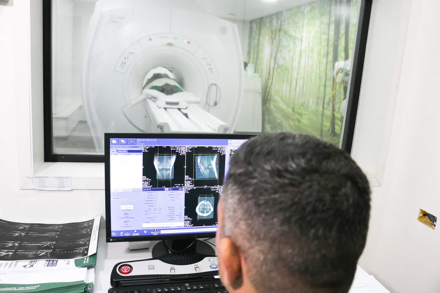 Técnico acompanha um exame de ressonância magnética pela sala de comando